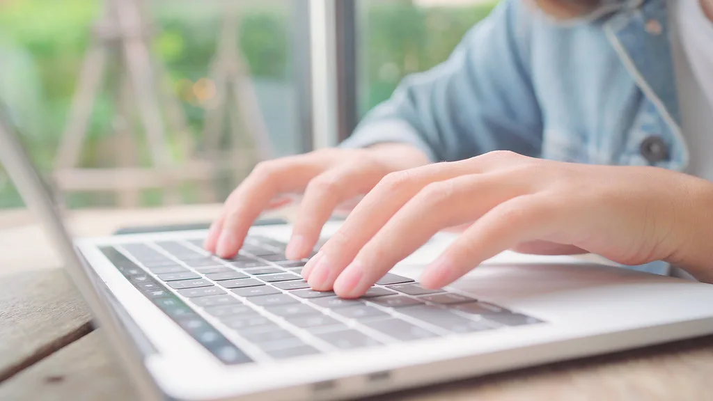 Mulher digitando em um notebook sobre a mesa de um café, fazendo uma pesquisa na internet