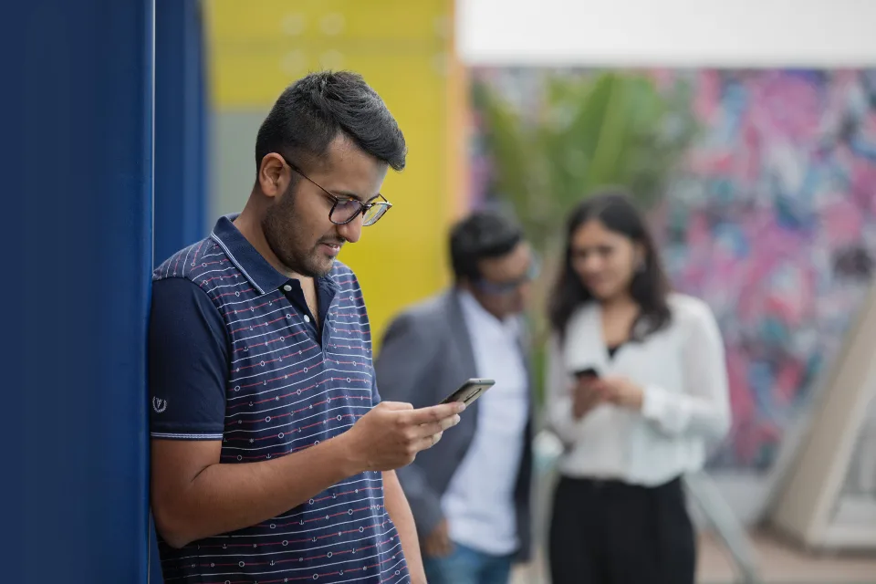 Pessoas em pé olhando o celular, uma delas digitando uma mensagem