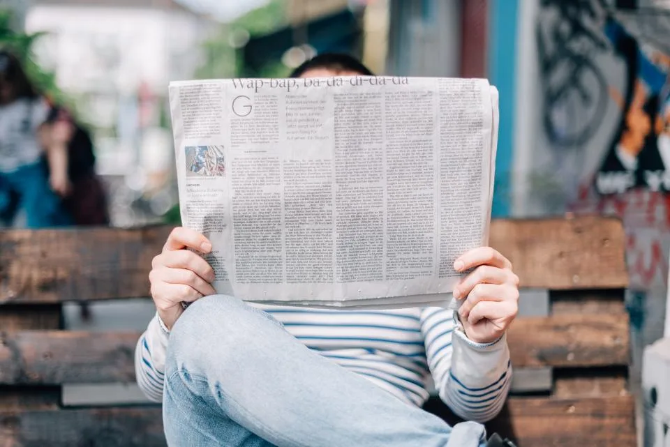 Homem lendo jornal aberto à mesa