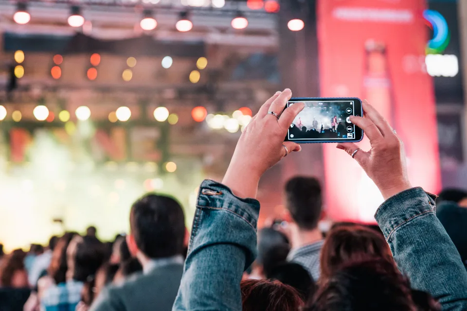 Participante filma o palco com o celular no meio do público de um evento