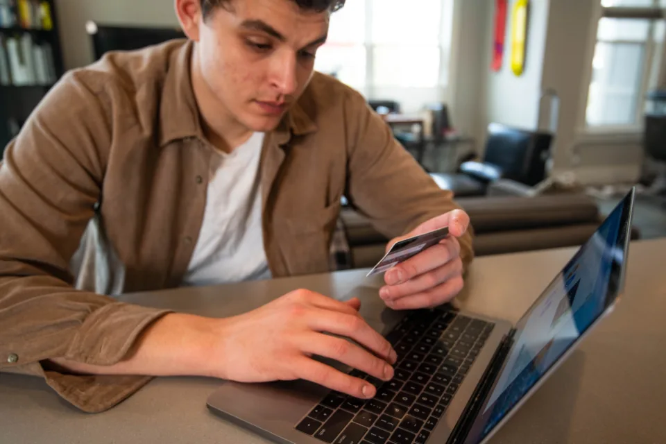 Homem com cartão na mão fazendo um pagamento no notebook