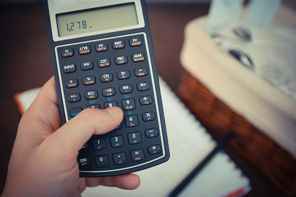 Mão segurando uma calculadora financeira sobre papéis