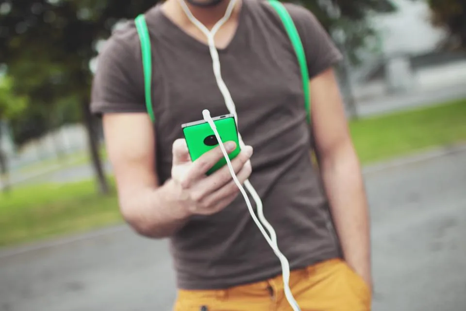 Rapaz com fones de ouvido mexendo num celular verde na rua
