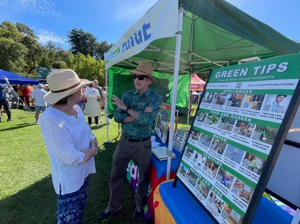 Visitantes conversando diante de um estande com painel de informações numa feira ao ar livre