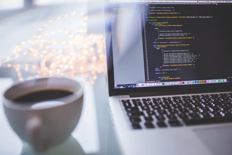 Notebook aberto com editor de código na tela, ao lado de uma xícara de café