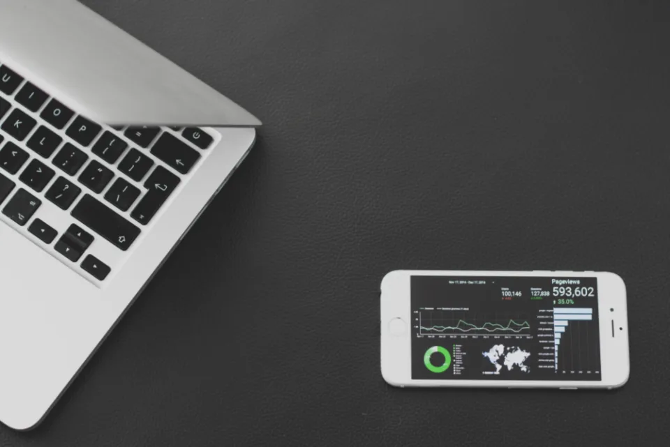 Notebook ao lado de um celular que mostra um painel de analytics com visualizações de página