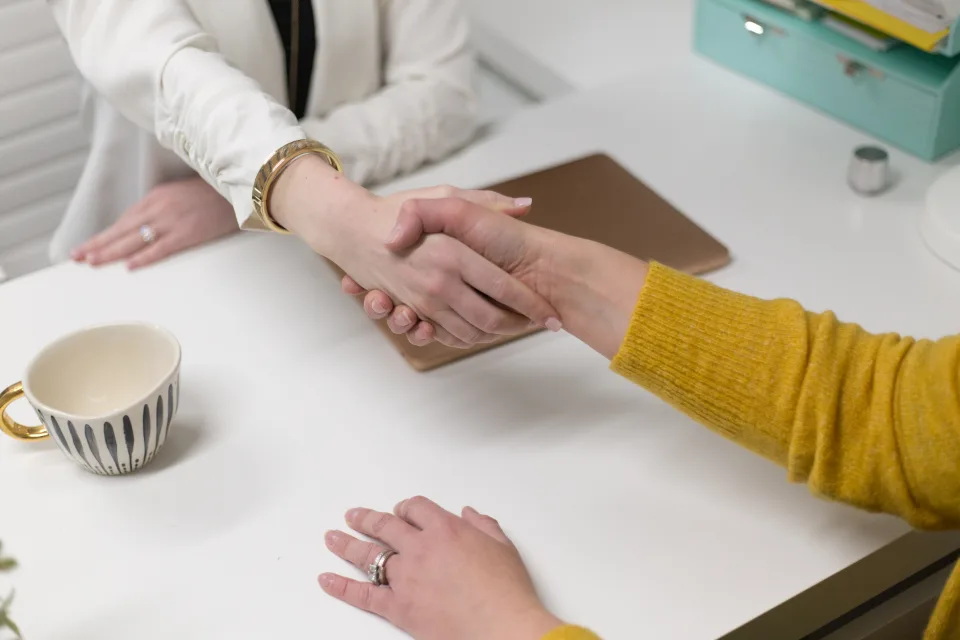 Duas pessoas apertando as mãos sobre uma mesa de reunião, ao fim de uma entrevista