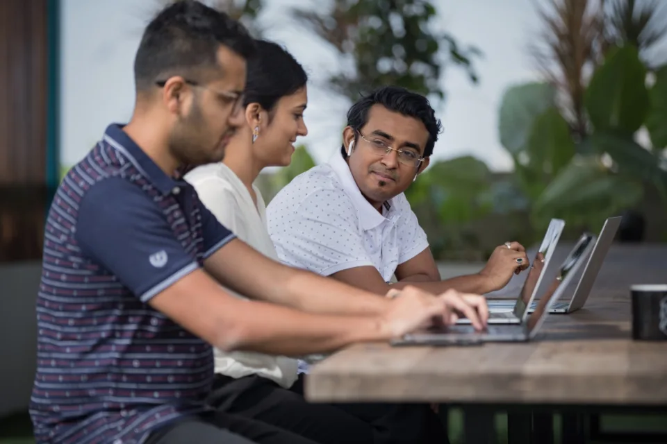 Colegas reunidos em volta de notebooks revisando dados de clientes numa mesa de trabalho