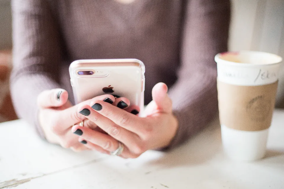 Pessoa segurando um celular ao lado de um copo de café, lendo mensagens