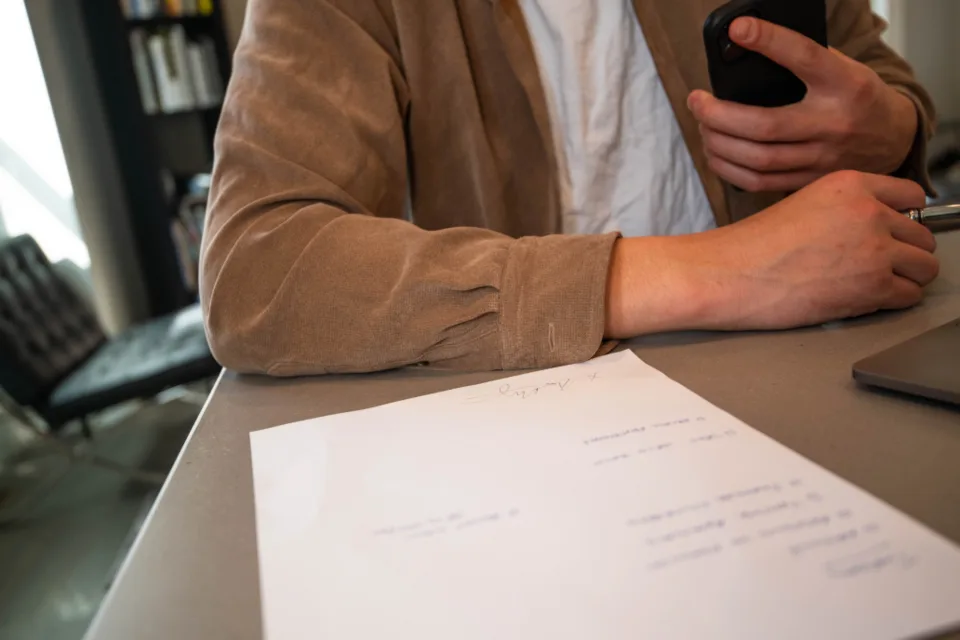 Pessoa revisando uma folha de contrato sobre a mesa, ao lado do notebook