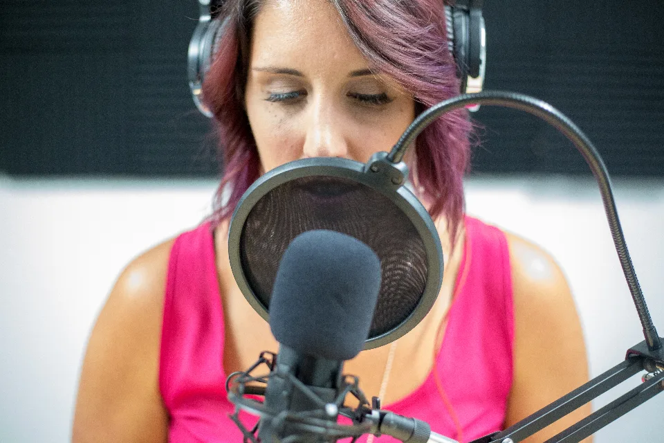 Mulher falando ao microfone em estúdio de gravação