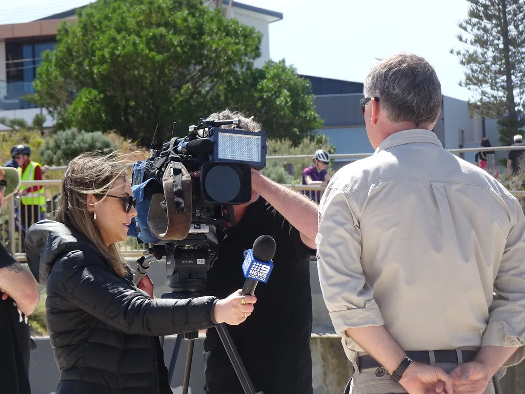 Equipe de televisão com câmera e microfone entrevistando um porta-voz ao ar livre