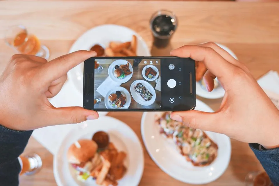 Mãos fotografando pratos de comida com o celular para as redes sociais
