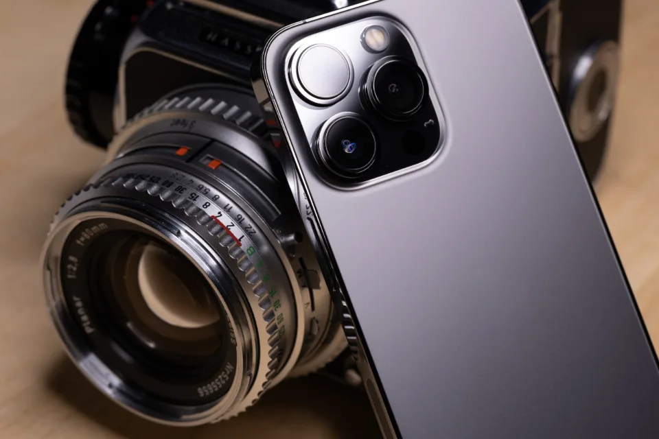 Smartphone com câmera tripla ao lado de uma câmera fotográfica, as ferramentas de trabalho de quem produz conteúdo