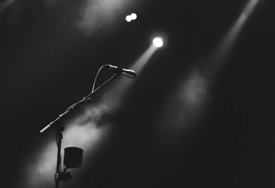 Microfone em pedestal sob a luz de refletores num palco escuro