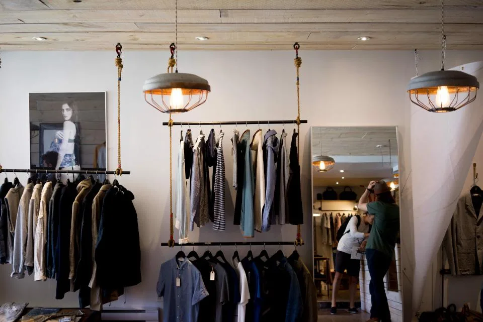 Interior de loja de roupas com araras de camisas e casacos e clientes se olhando no espelho