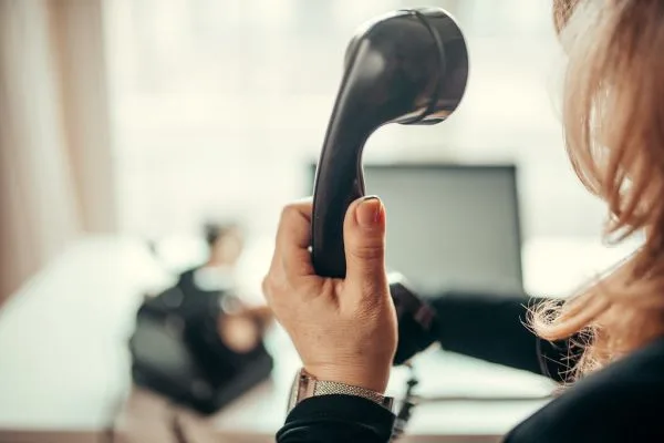 Mão segurando o fone de um telefone de mesa no escritório