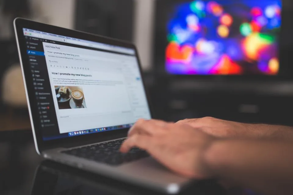 Mãos digitando em notebook com o editor de um blog aberto na tela