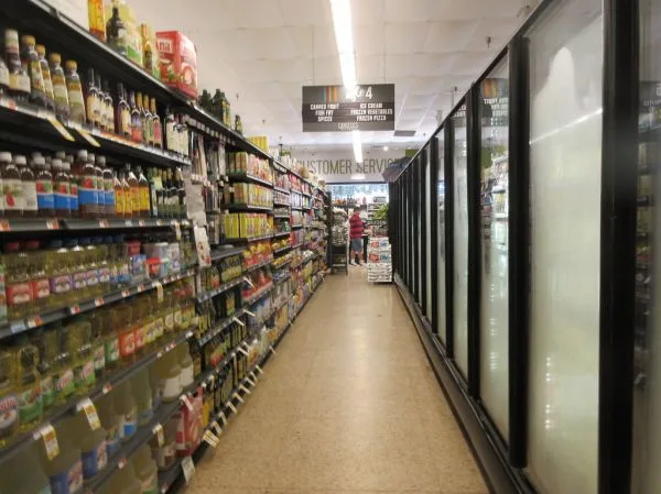 Corredor de supermercado com prateleiras abastecidas e geladeiras à direita