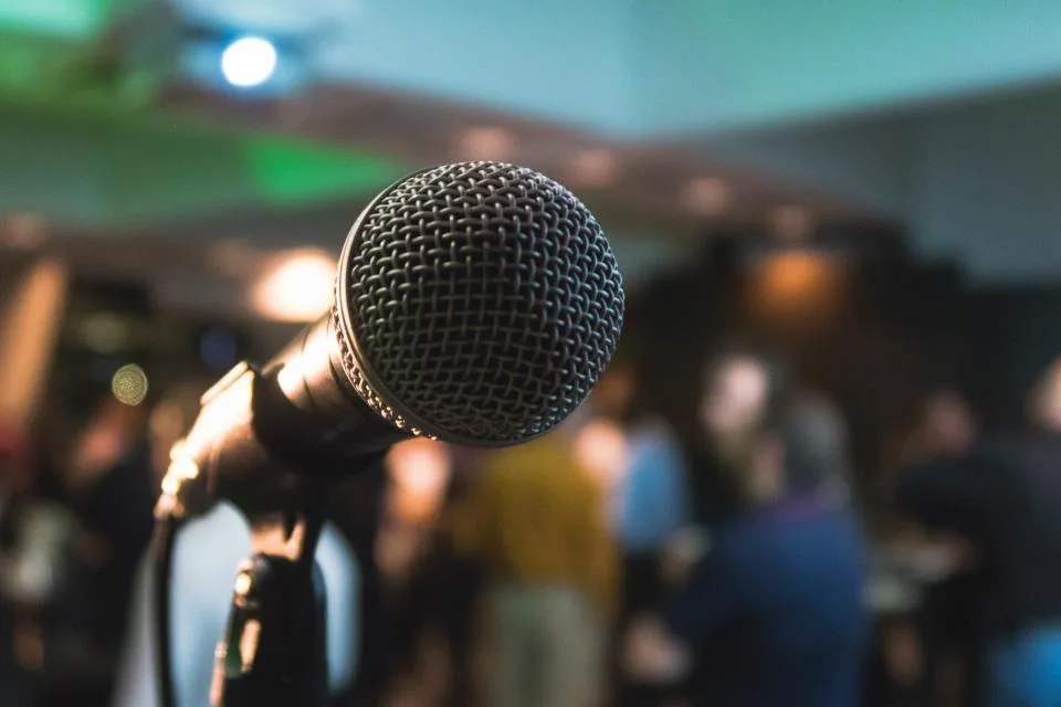 Microfone em primeiro plano numa sala com público ao fundo