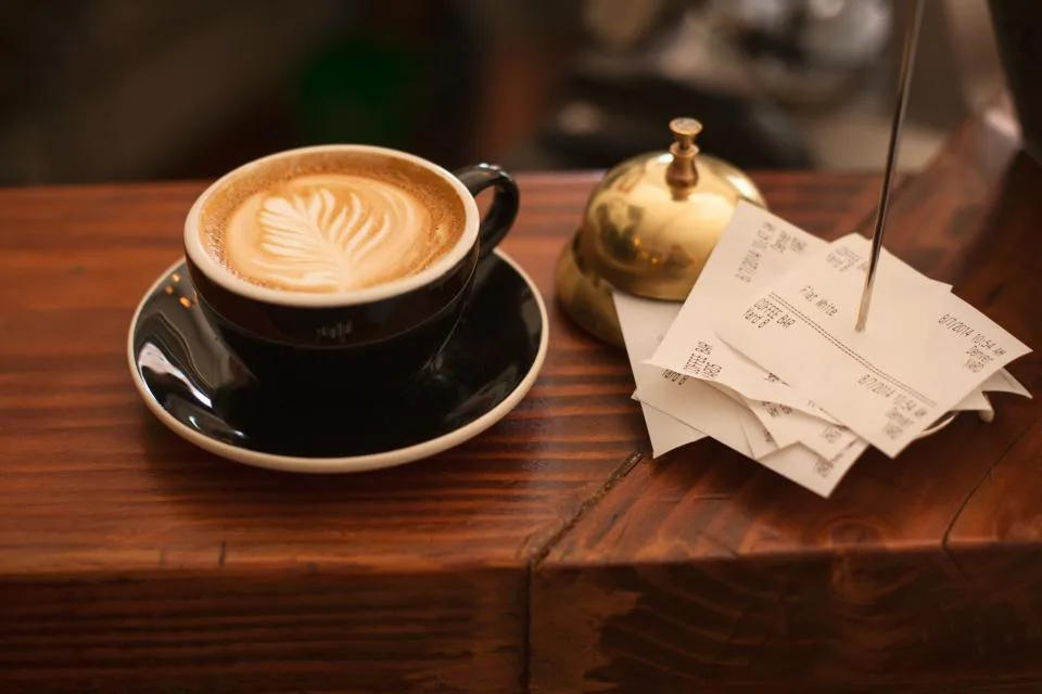 Xícara de café com arte no leite ao lado de comprovantes de compra no balcão