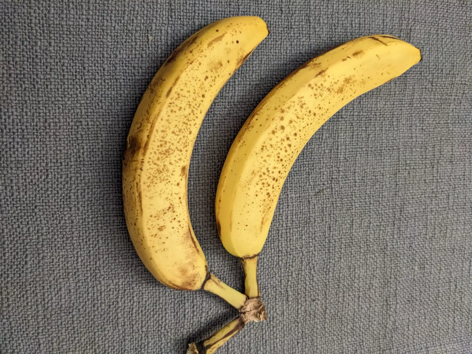 Duas bananas lado a lado sobre um tecido cinza
