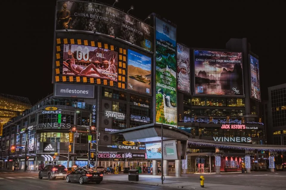 Fachadas cobertas de painéis publicitários iluminados numa rua comercial à noite