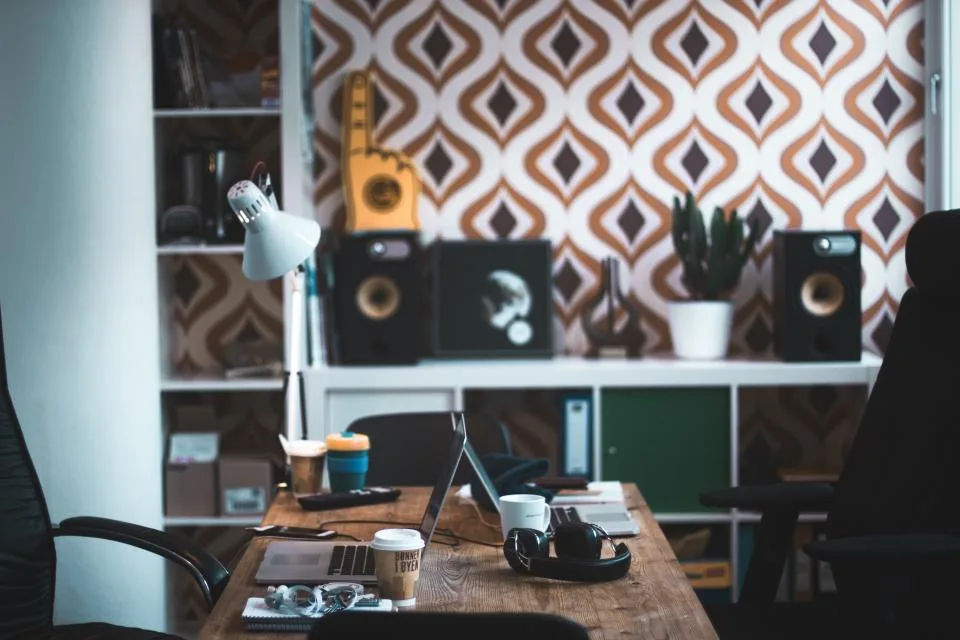 Mesa de escritório com notebooks abertos, fones de ouvido e estante ao fundo