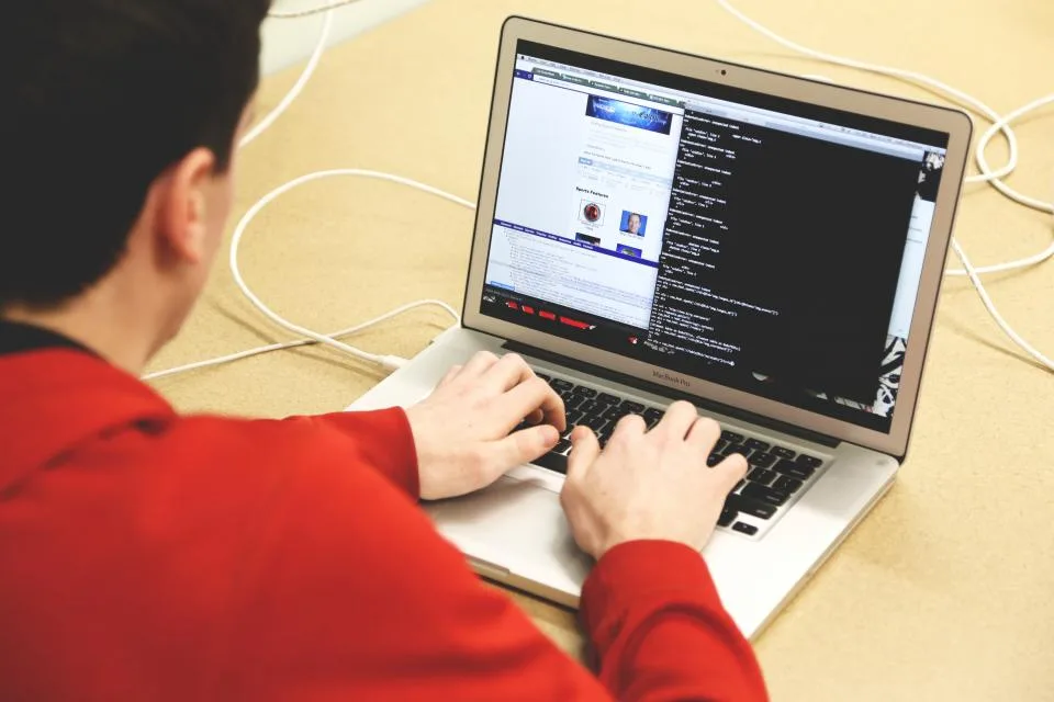 Programador escrevendo código em um notebook sobre a mesa