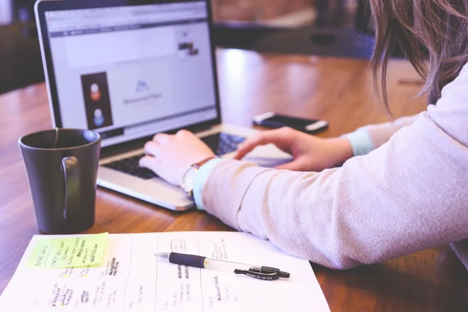 Pessoa trabalhando num notebook sobre a mesa, com xícara e anotações ao lado