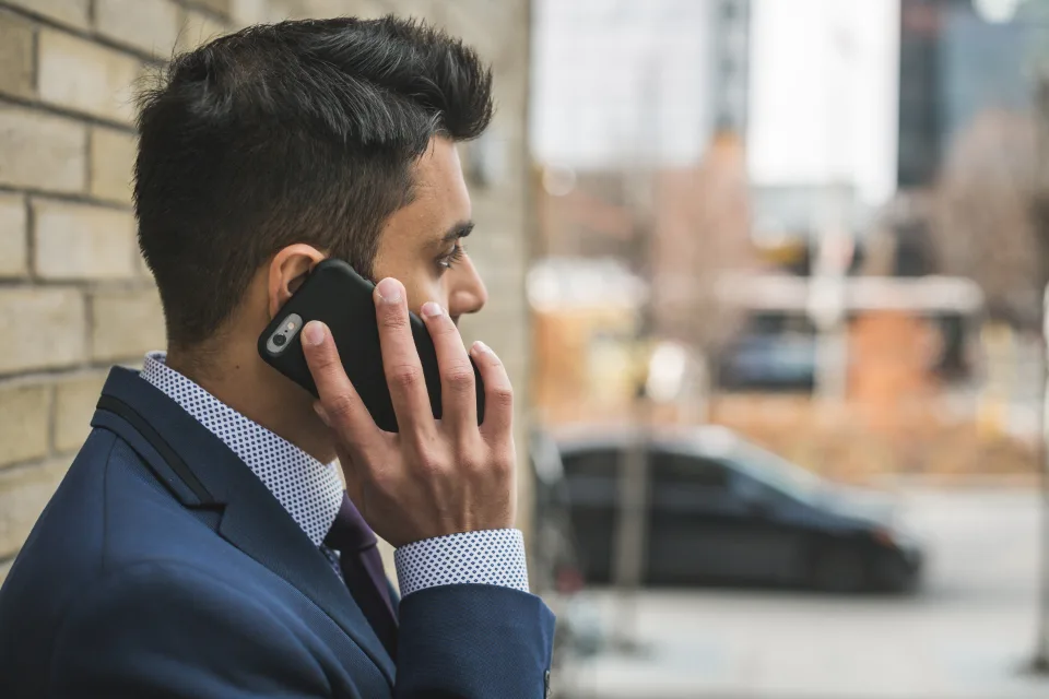 Homem de terno falando ao celular na rua, representando o atendimento que responde ao cliente