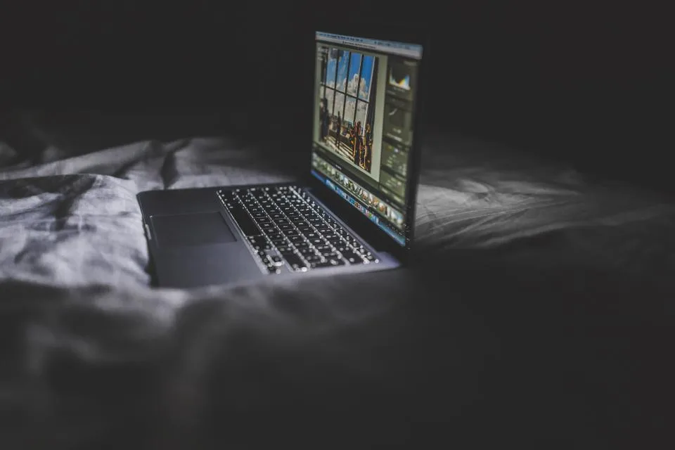Notebook aberto com a tela acesa num quarto escuro, sugerindo uso fora do horário e do controle da empresa