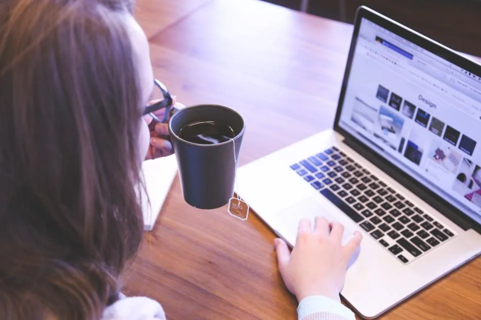 Mulher navegando em um site pelo notebook com café ao lado