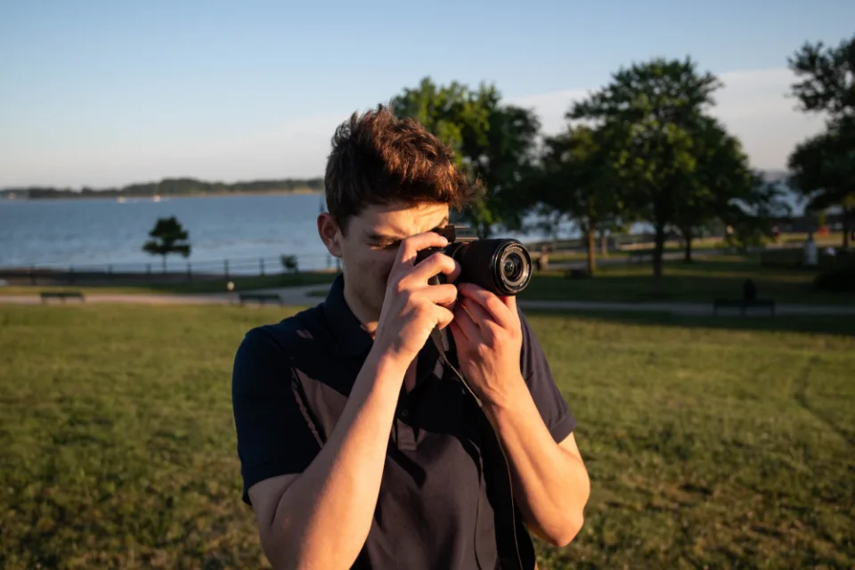 Fotógrafo ao ar livre enquadrando uma foto com câmera analógica, com um lago ao fundo