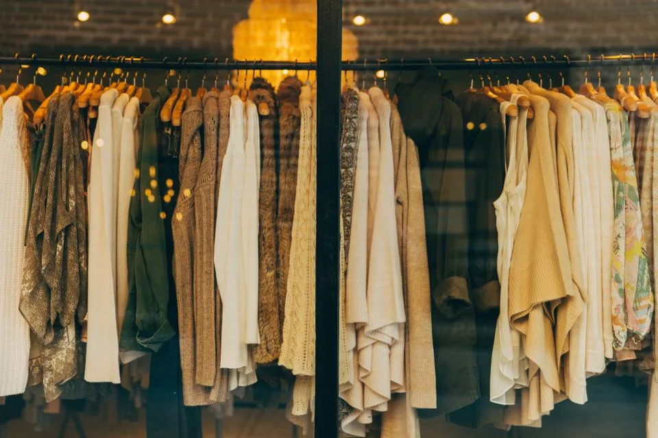 Vitrine de loja de roupas vista da rua, com araras de peças bem iluminadas atrás do vidro