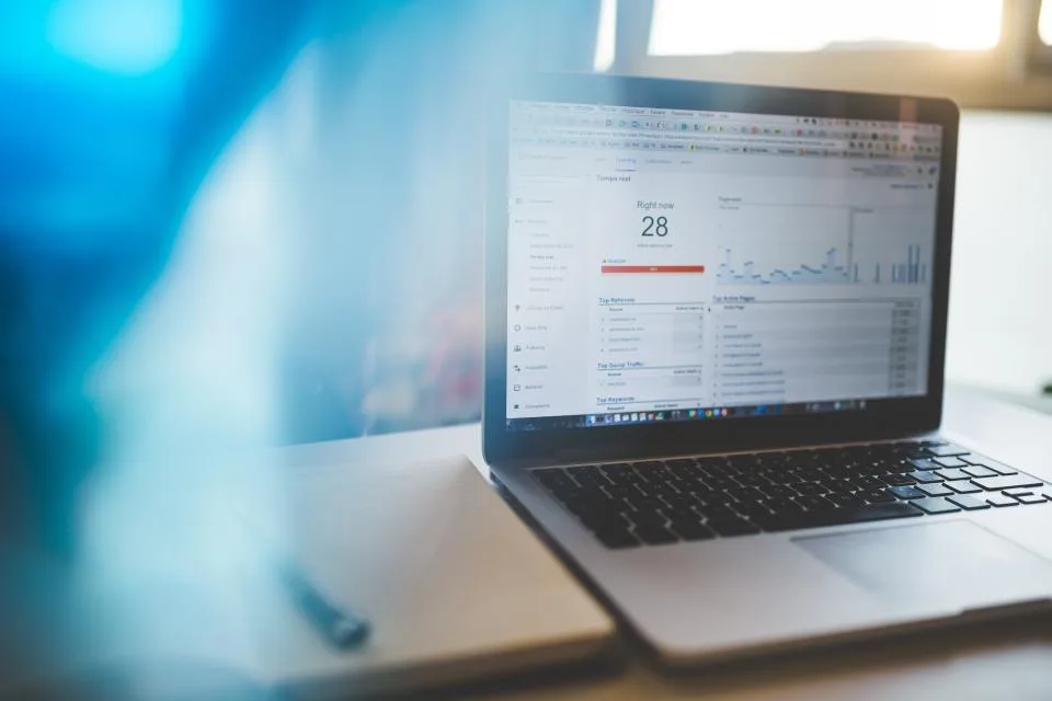 Notebook aberto com gráficos de acesso de um site na tela, sobre fundo azul